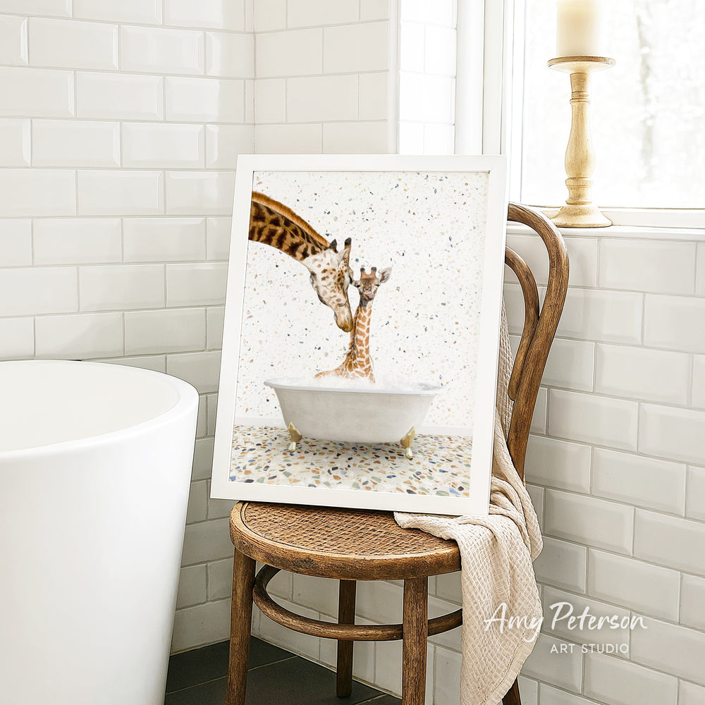 A framed image of two giraffes standing in a bathtub, with one giraffe appearing to be bathing the other giraffe. The image is displayed on a wooden chair in a bathroom setting.