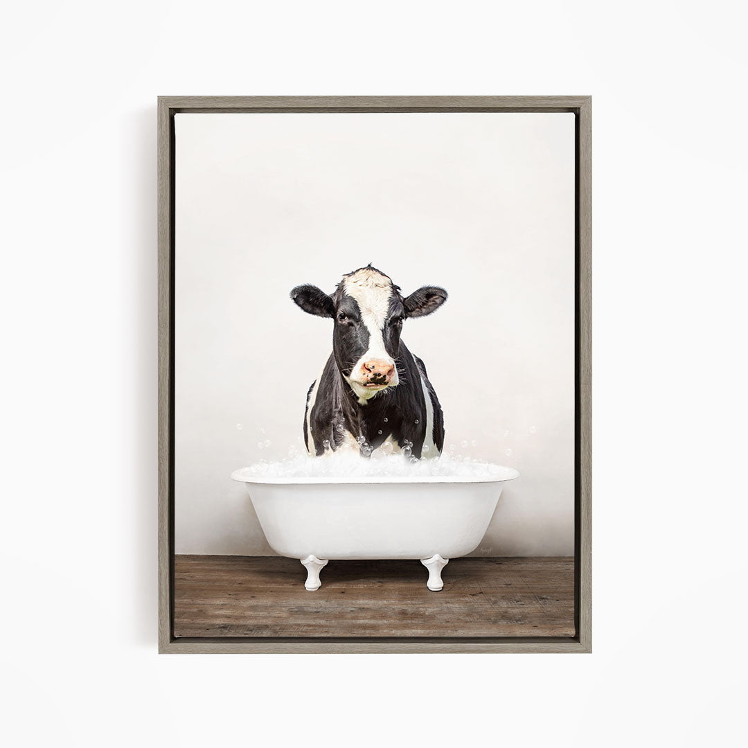 A black and white cow is sitting in a white bathtub filled with water, creating a whimsical and humorous scene.