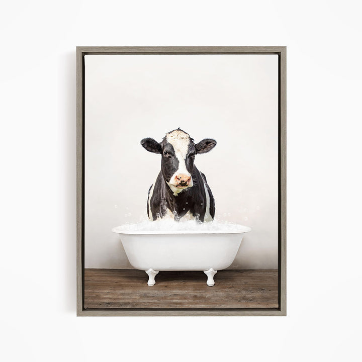 A black and white cow is sitting in a white bathtub filled with water, creating a whimsical and humorous scene.