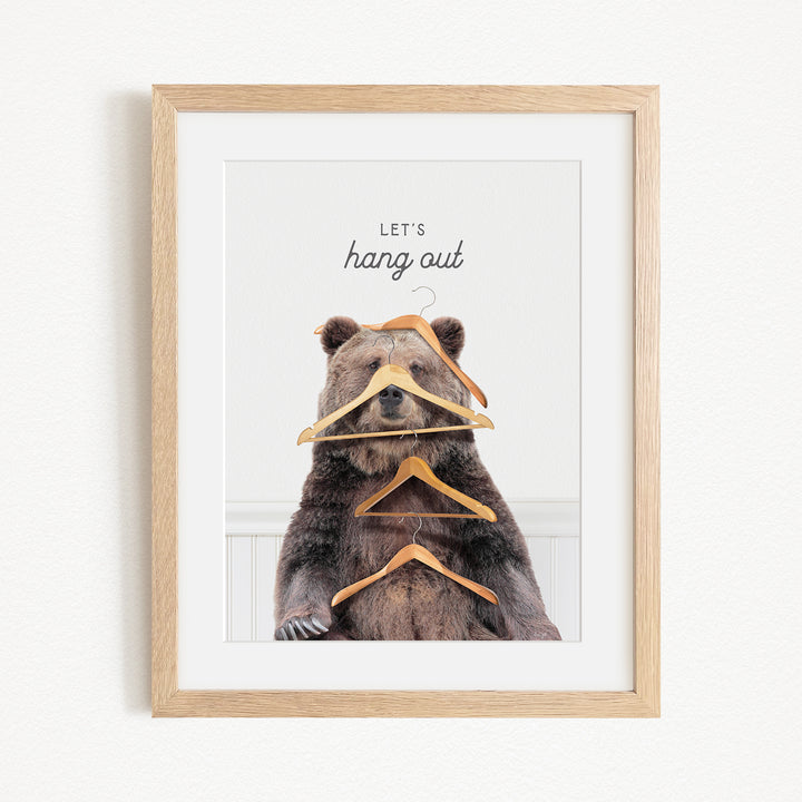 A framed image of a bear sitting on a shelf with a pile of clothes hanging from its head.