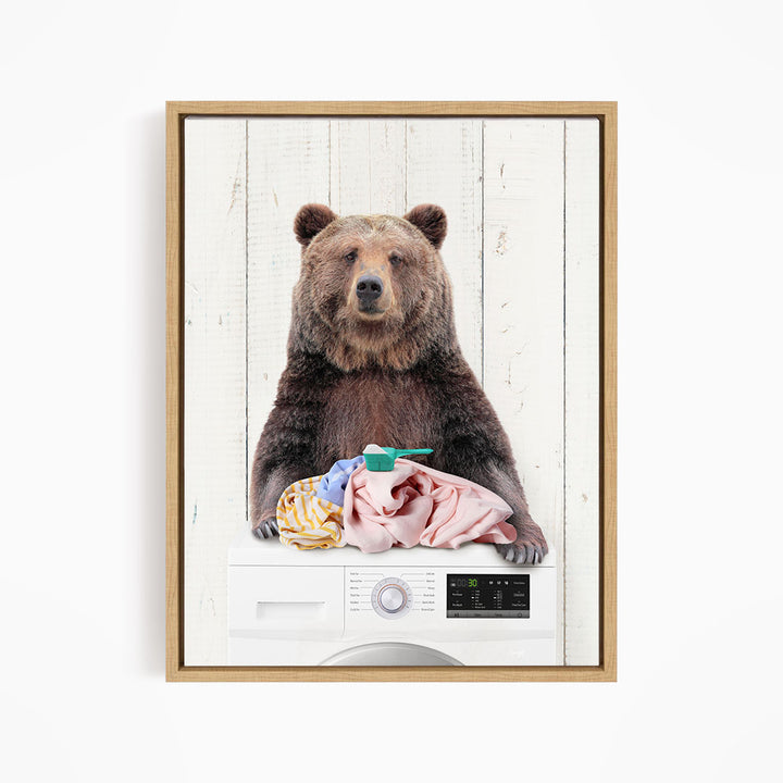A brown bear sitting on top of a washing machine, holding a pile of clothes.