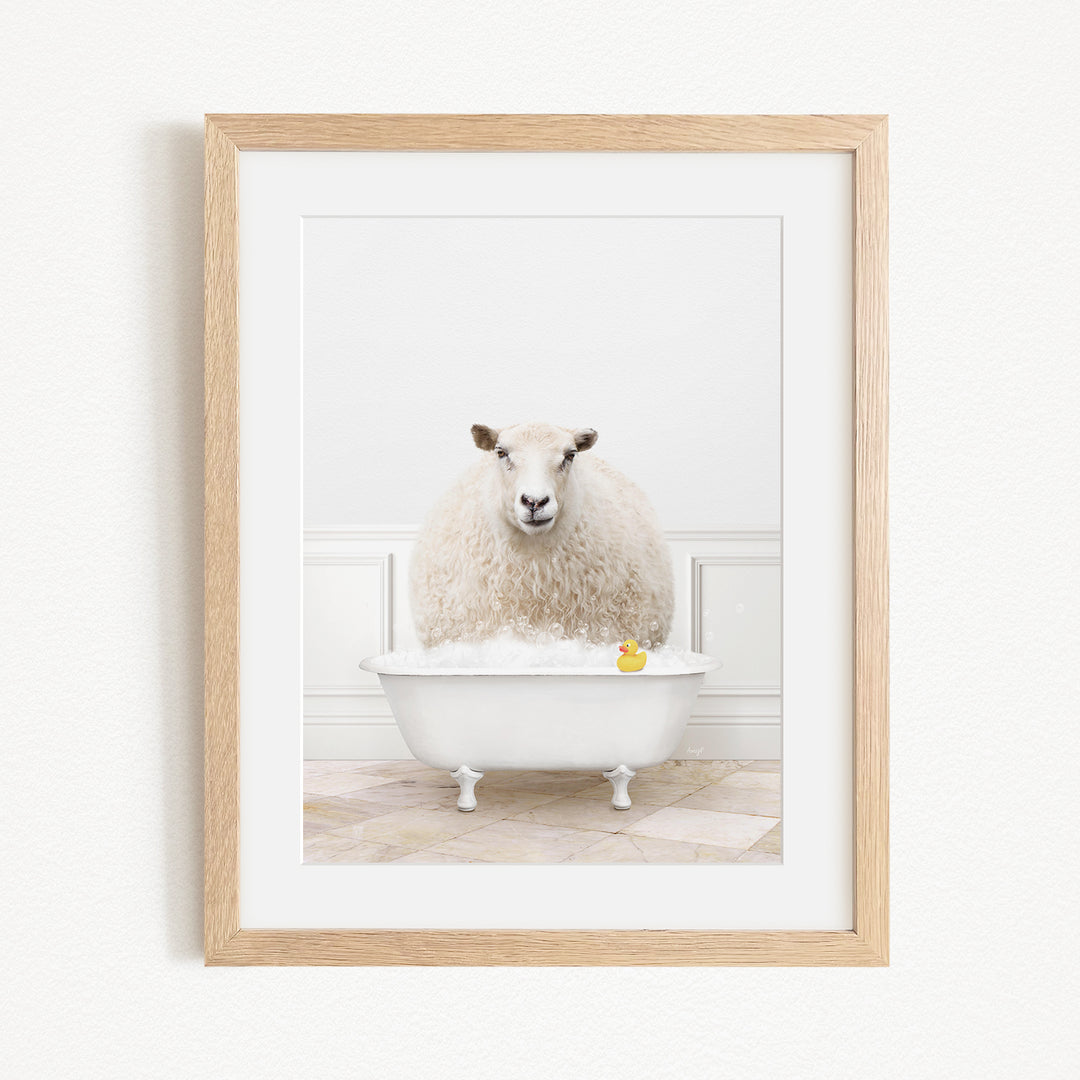 A fluffy white sheep sits in a white bathtub filled with bubbles, with a yellow rubber duck floating in the water.