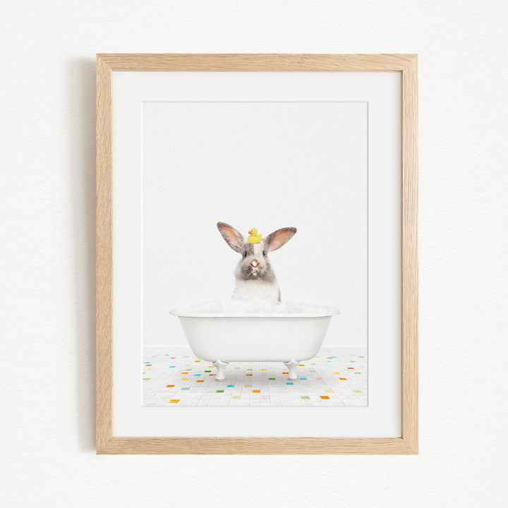 A white rabbit sitting in a white bathtub filled with bubbles, with a yellow duck perched on its head.