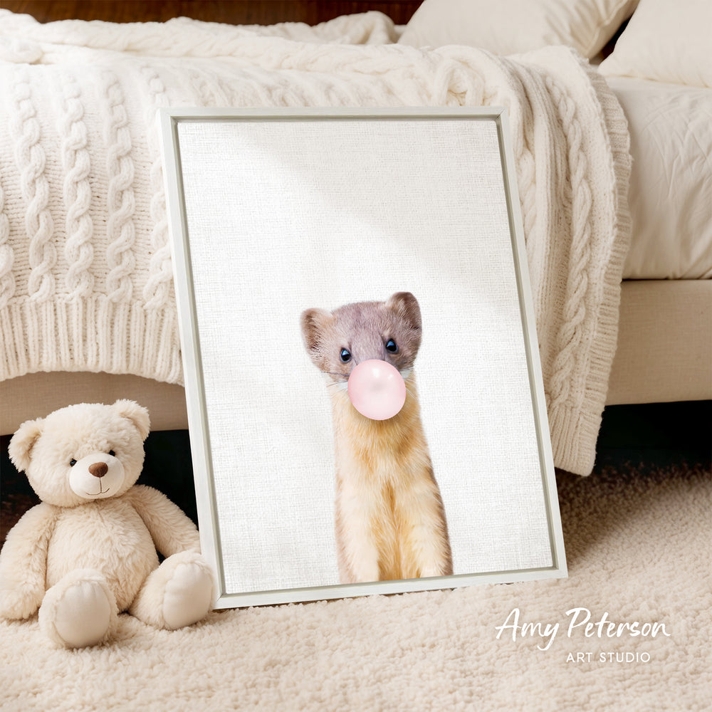 A framed image of a brown and white ferret blowing a bubble gum bubble is displayed on a white wall, accompanied by a teddy bear on a beige carpet.