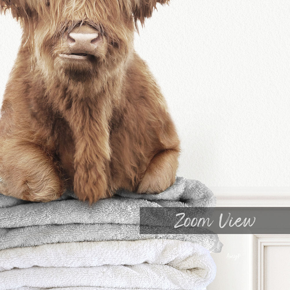 A close-up of a brown furry animal, possibly a yak or a cow, sitting on top of a stack of towels.