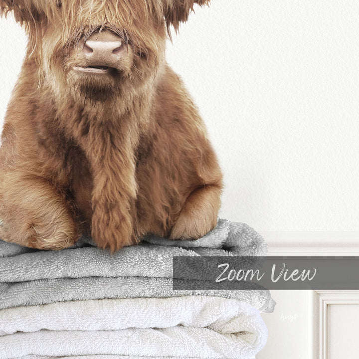 A close-up of a brown furry animal, possibly a yak or a cow, sitting on top of a stack of towels.
