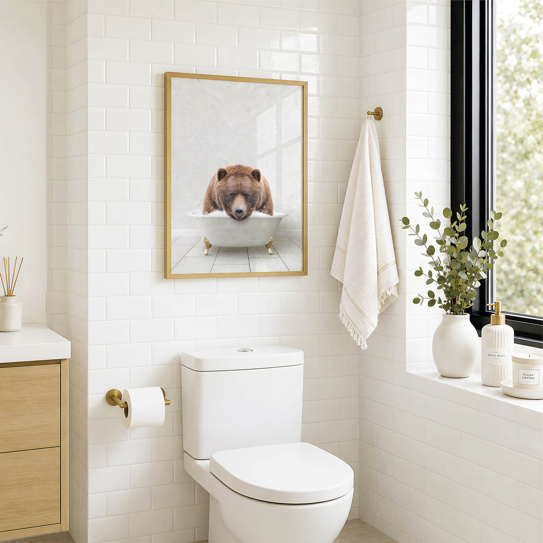 A bathroom with a white toilet, a framed image of a bear sitting in a bathtub, and a window with greenery outside.