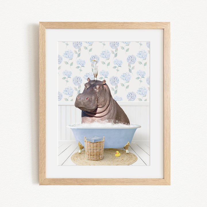 A framed image depicting a hippopotamus sitting in a bathtub filled with water, surrounded by a blue floral pattern on the wall.