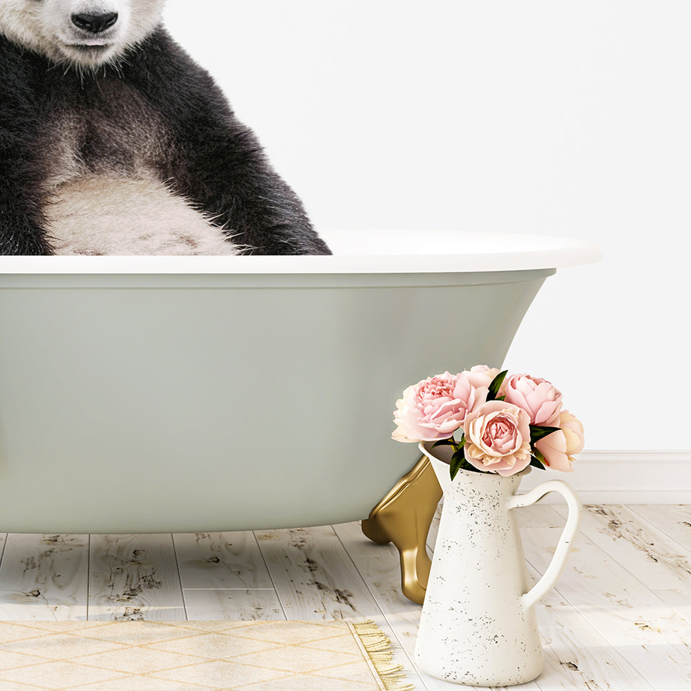 A panda sitting in a green bathtub, with a vase of pink flowers next to it on a wooden floor.