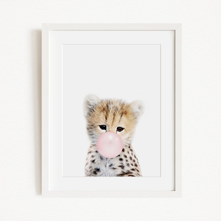 A cute cheetah with spotted fur blowing a bubble with a pink bubble gum bubble.