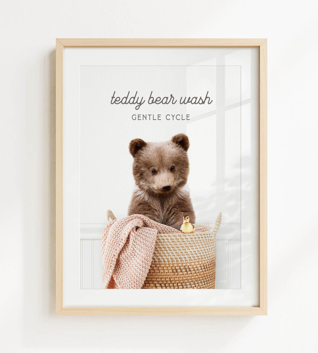 A framed image of a teddy bear sitting in a woven basket, with a small yellow duck peeking out from the basket.