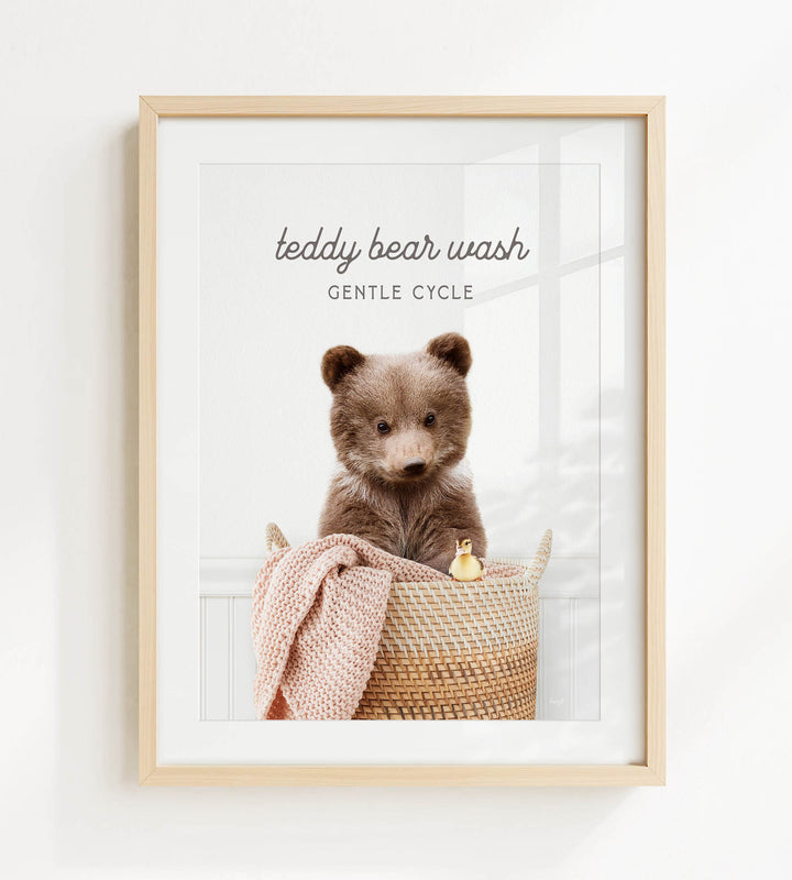 A framed image of a teddy bear sitting in a woven basket, with a small yellow duck peeking out from the basket.