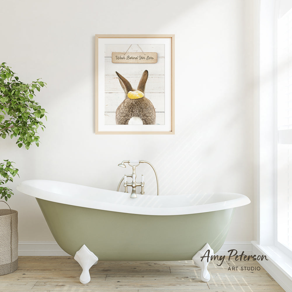 a bathroom with a green clawfoot bathtub, a framed picture of a rabbit, and a potted plant.
