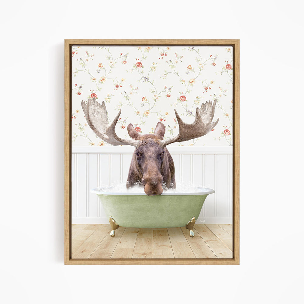 A moose with large antlers is sitting in a green bathtub, surrounded by a floral wallpaper.