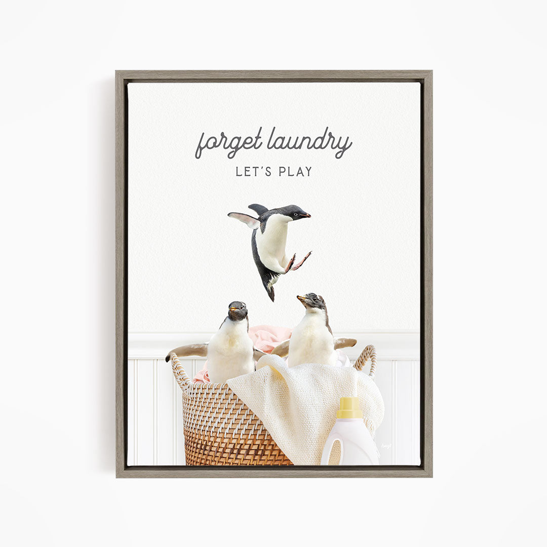 A framed image depicting three penguins in a laundry basket, with the text "forget laundry let's play" written above them.