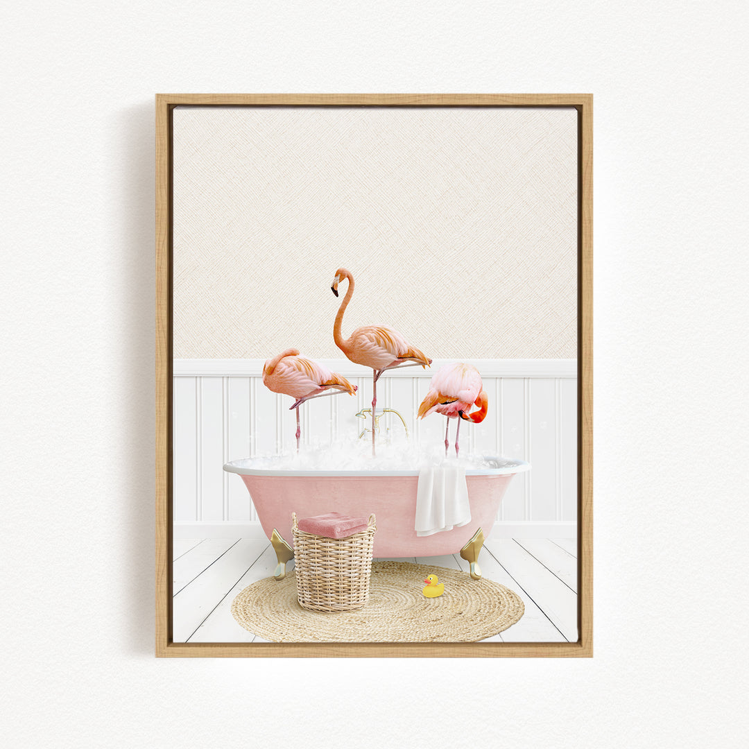 A framed image depicting three flamingos standing in a pink bathtub filled with bubbles, surrounded by a basket of bath toys and a yellow rubber duck.