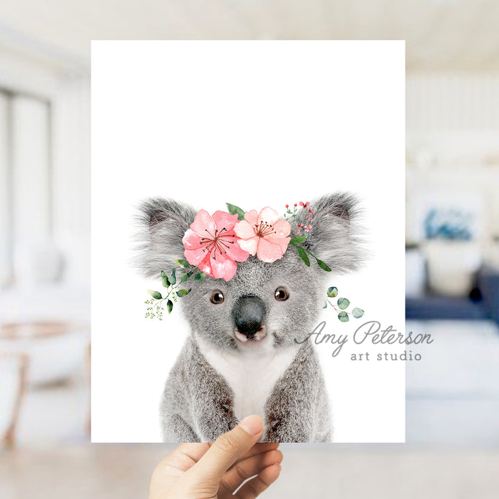 a hand holding up a card with a koala bear wearing a flower crown