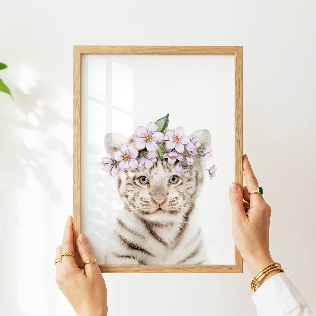 A person's hands are holding a picture frame with a photograph of a tiger wearing a flower crown.