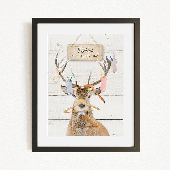 A framed print depicting a deer with antlers holding various laundry items, including socks and clothes hangers, with a sign above that says "I Harded It's Laundry Day".
