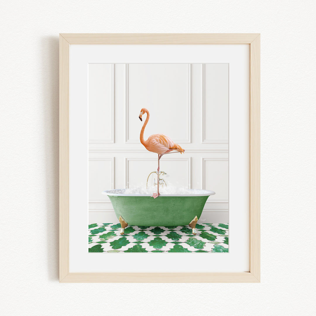 A framed image of a pink flamingo standing on the edge of a green bathtub filled with water, set against a white wall with a green and white patterned rug.