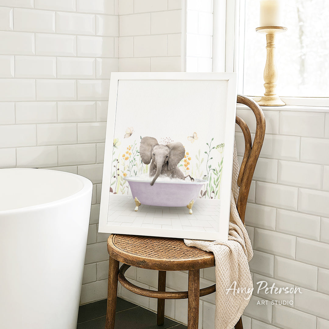 A framed illustration of an elephant sitting in a bathtub, surrounded by flowers, is displayed on a wooden chair in a bathroom setting.