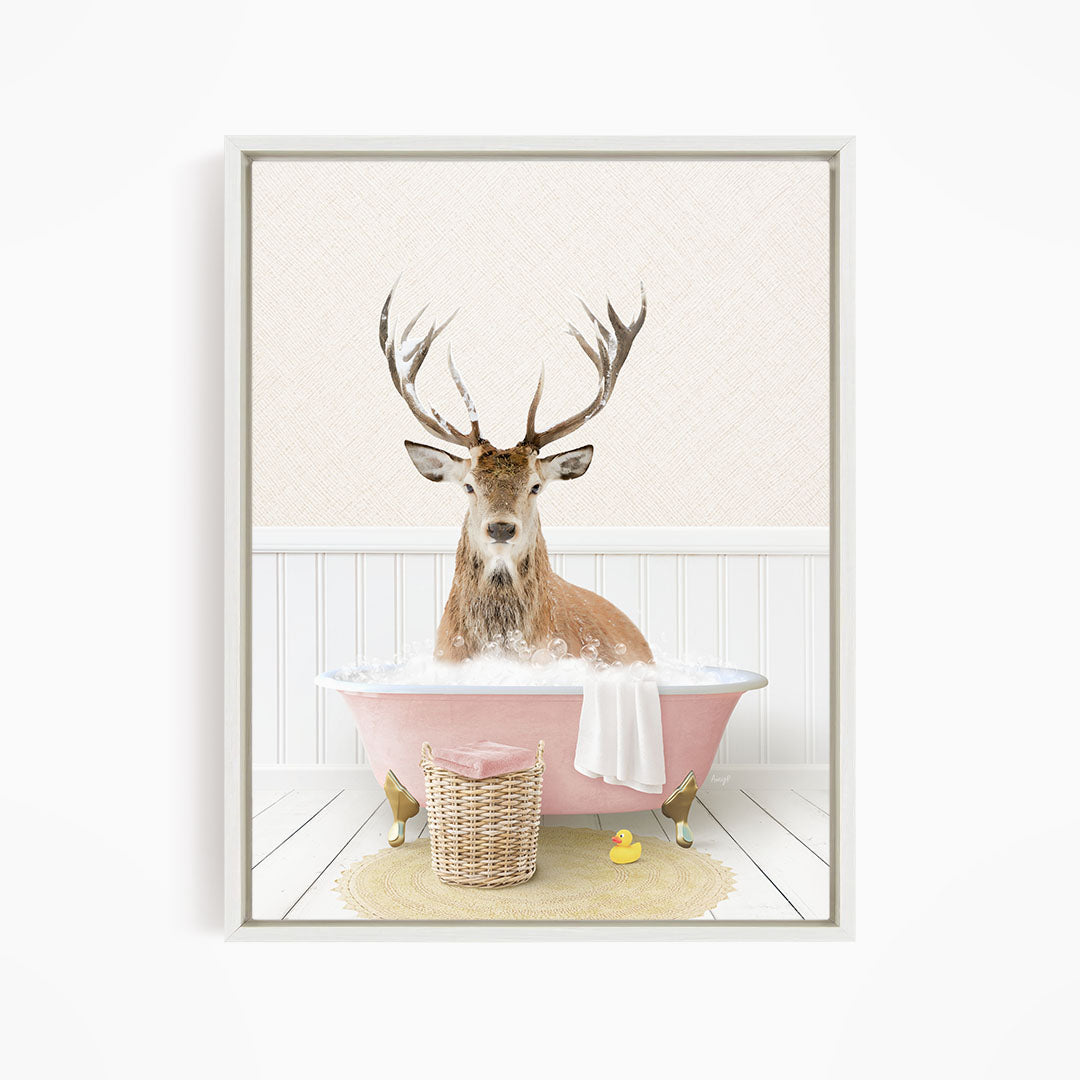 A deer with antlers is sitting in a pink bathtub filled with bubbles, surrounded by a yellow rubber duck and a wicker basket.