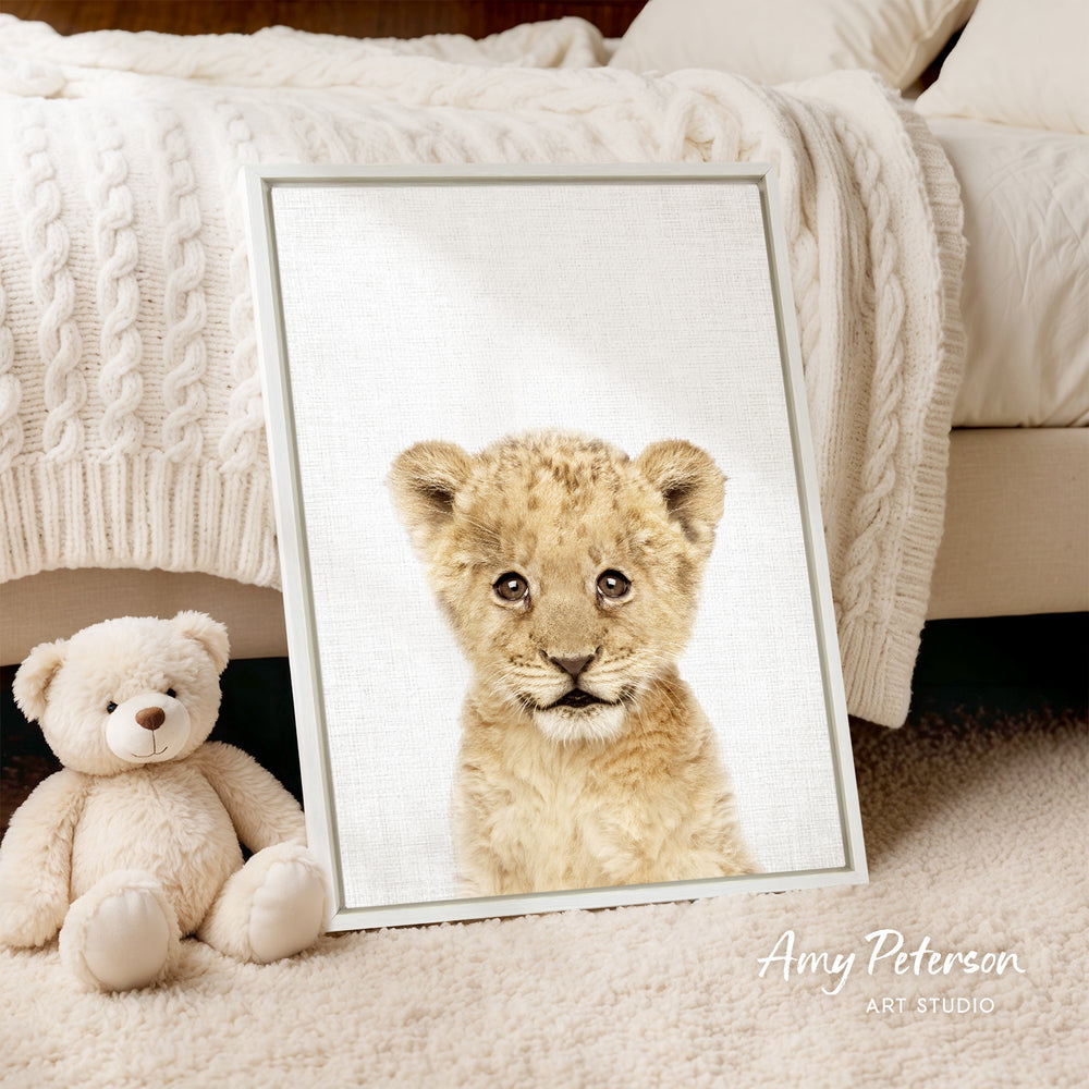 A framed photograph of a young lion cub is displayed on a bed, accompanied by a teddy bear.