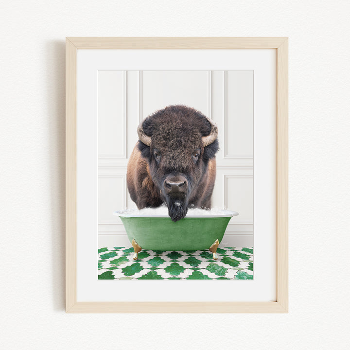 A buffalo with a black nose and brown fur is standing in a green bathtub filled with water, with a green and white patterned rug on the floor.