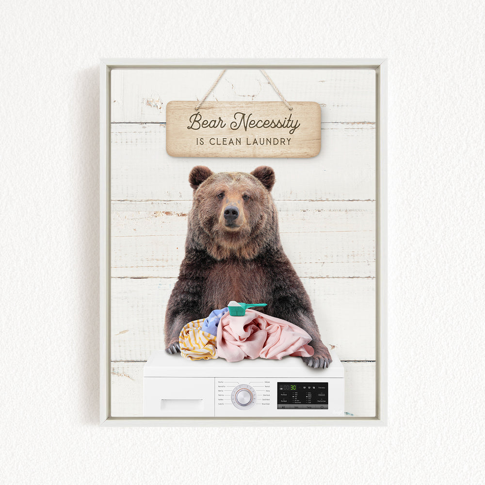 A framed image of a brown bear sitting on a washing machine, with a sign above that says "Bear Necessity is Clean Laundry".