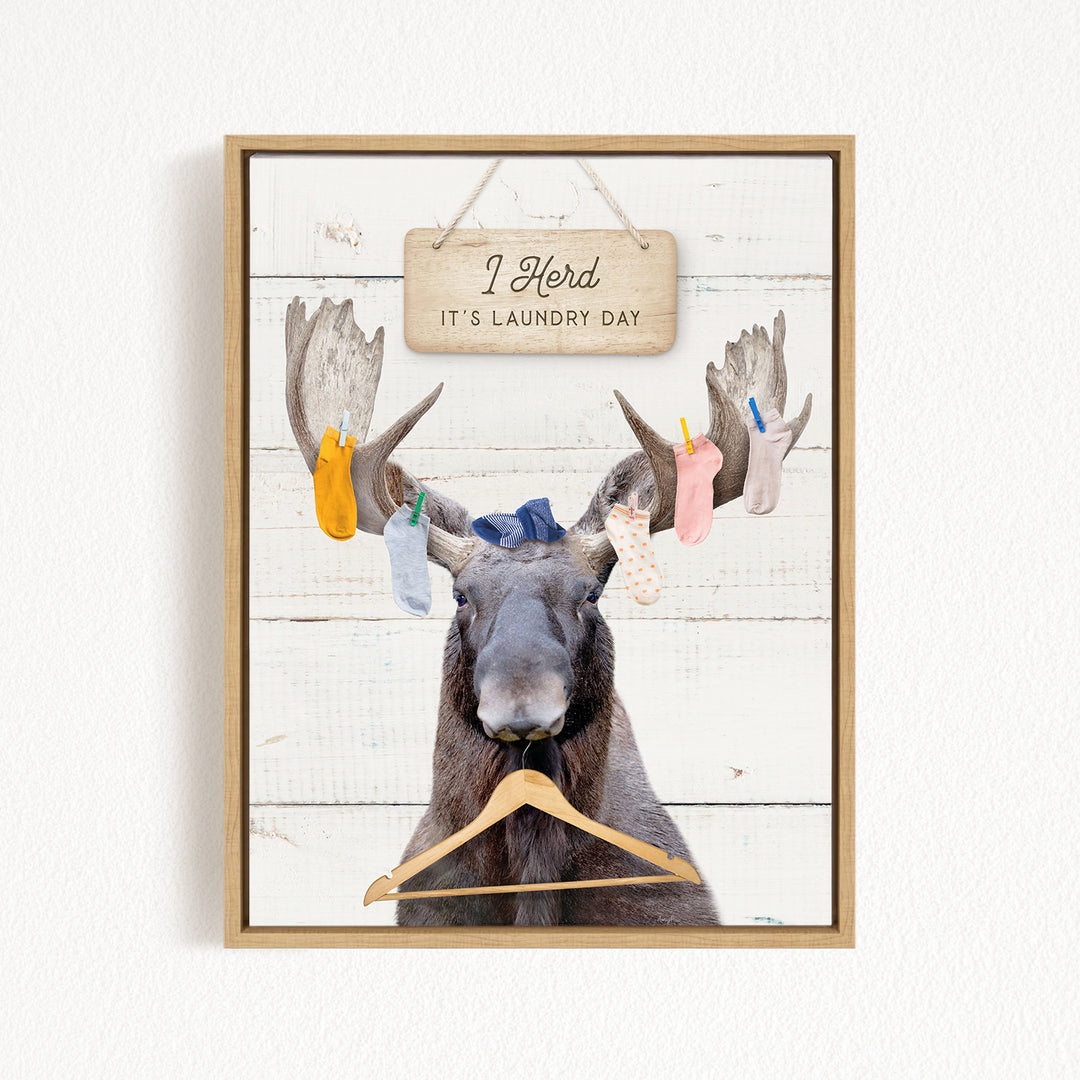 A framed image depicting a moose with a sign above its head that says "I herd it's laundry day".