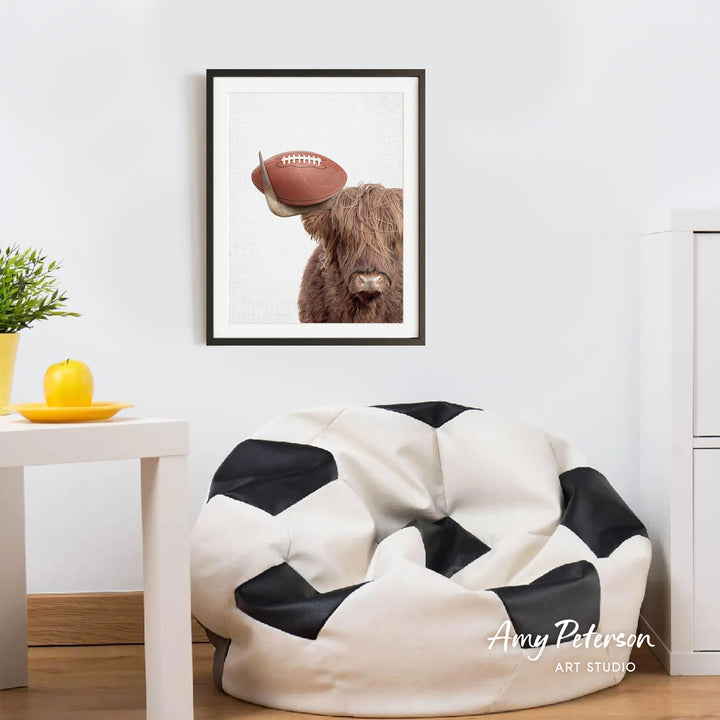 a framed picture of a cow with a football on its head, hanging on a wall above a white bean bag chair.