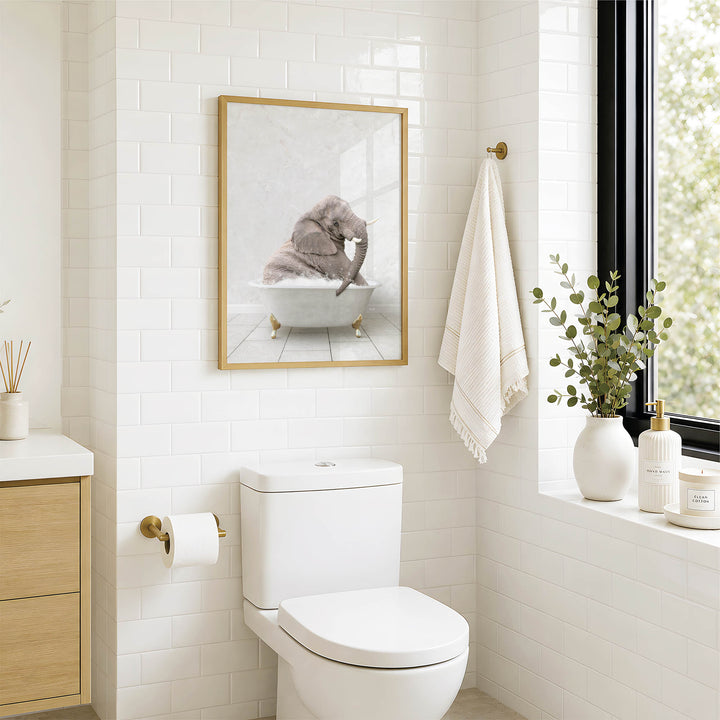 A bathroom with a white toilet, a framed picture of an elephant in a bathtub, and a window with greenery on the sill.