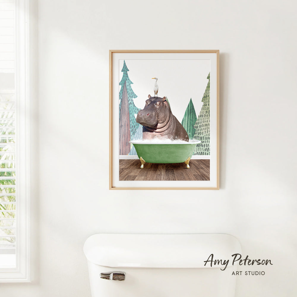 A framed illustration of a hippopotamus sitting in a green bathtub, surrounded by trees and a bird, is displayed on a white wall.