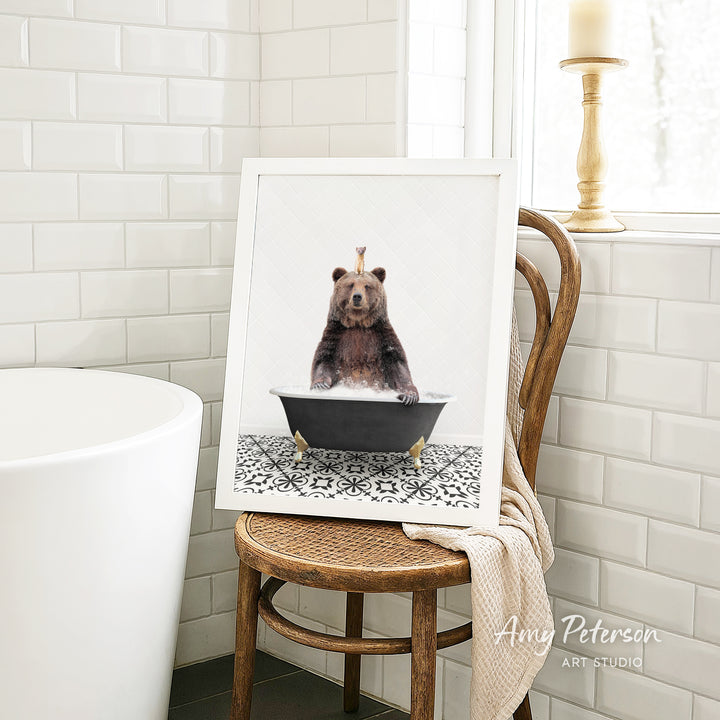 A framed image of a bear sitting in a bathtub, with a crown on its head, is displayed on a wooden chair in a bathroom setting.