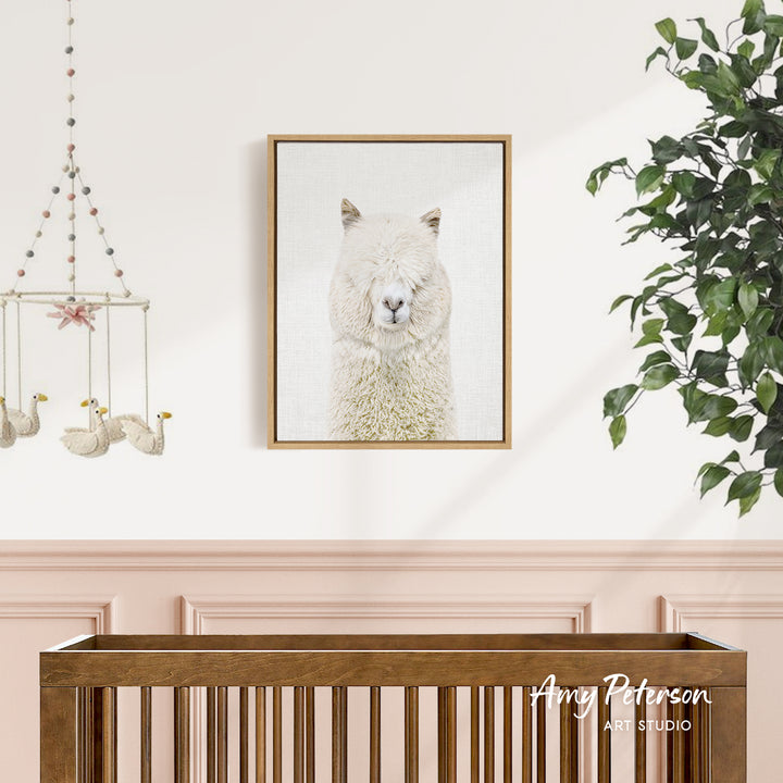 a framed picture of a white llama hanging on a wall above a wooden crib.
