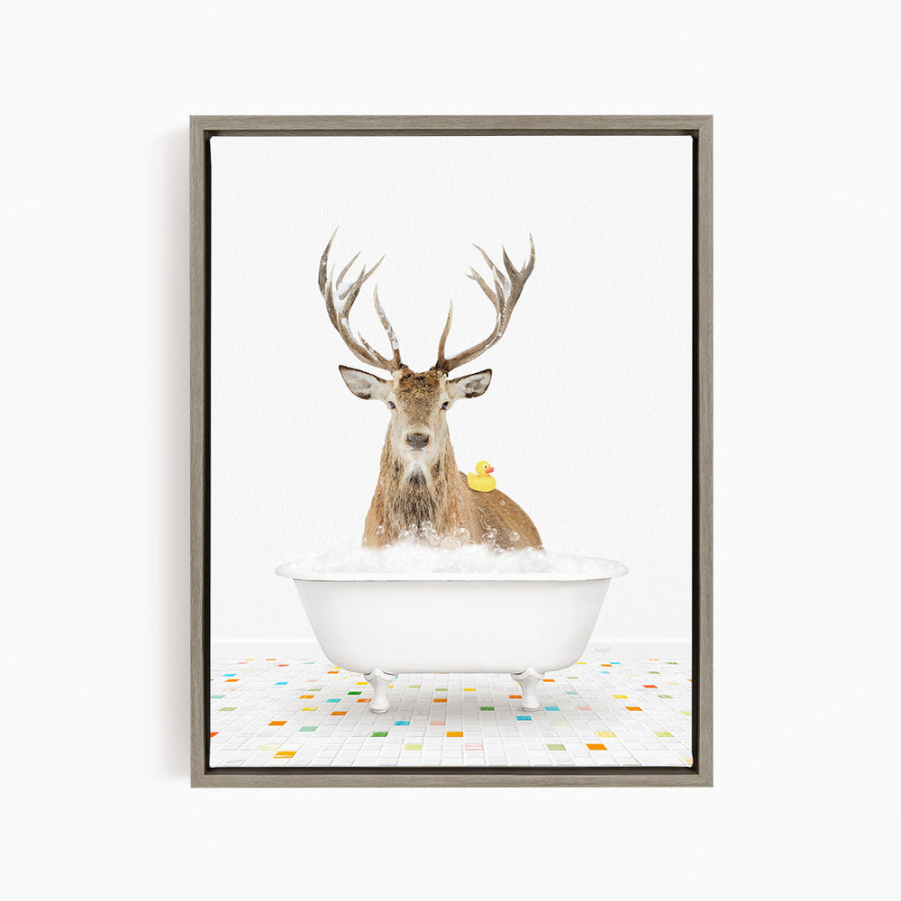 A deer with large antlers is sitting in a white bathtub filled with bubbles, with a yellow rubber duck resting on its back.