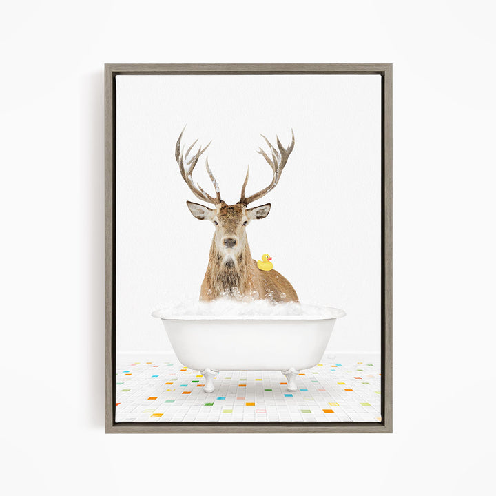 A deer with large antlers is sitting in a white bathtub filled with bubbles, with a yellow rubber duck resting on its back.