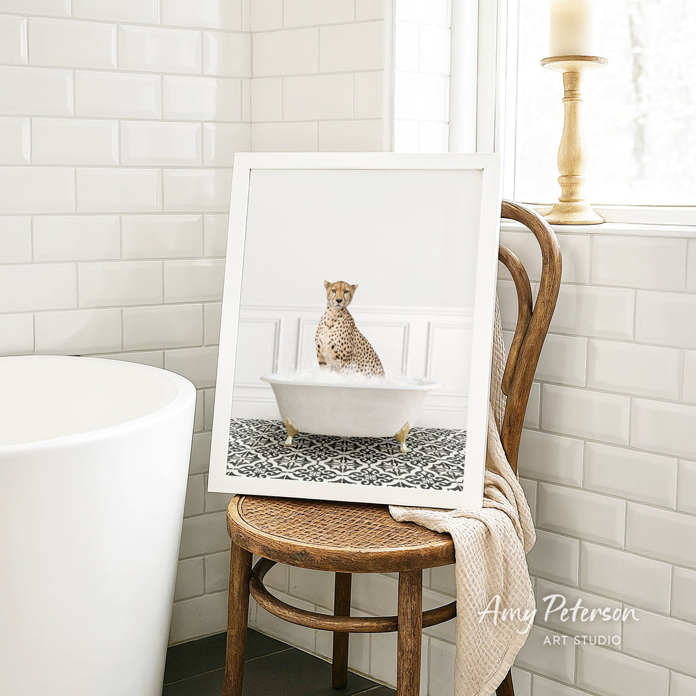 A cheetah sitting in a bathtub, as depicted in a framed artwork, is placed on a wooden chair in a bathroom setting.