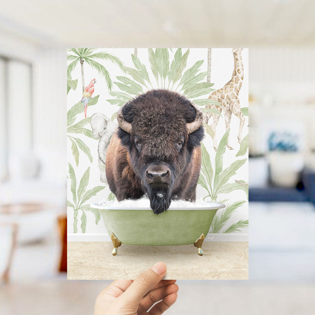 A hand holds up a framed print featuring a close-up of a bison in a bathtub, surrounded by tropical foliage and a giraffe.