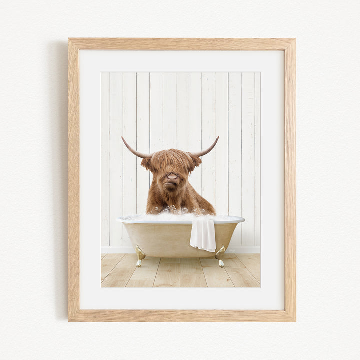 A brown Highland cow with large horns is sitting in a white bathtub, with a towel draped over the side of the tub.
