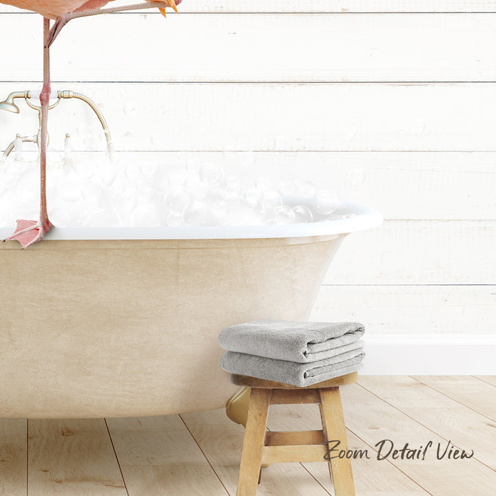 A white clawfoot bathtub filled with water and bubbles, with a pair of gray towels placed on a wooden stool next to it.