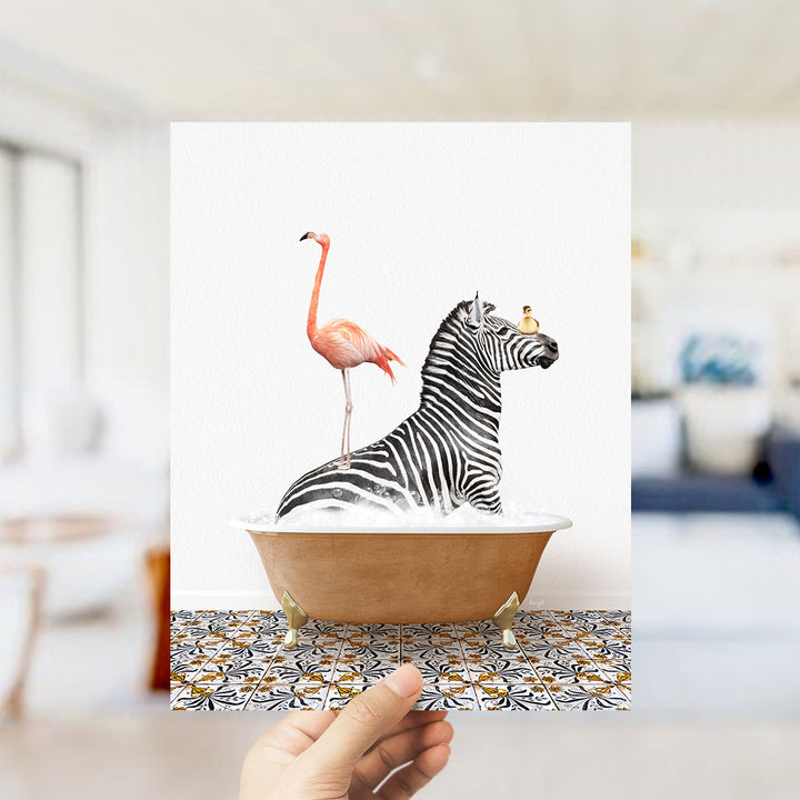 A hand holds up a framed image depicting a zebra standing in a bathtub with a pink flamingo.