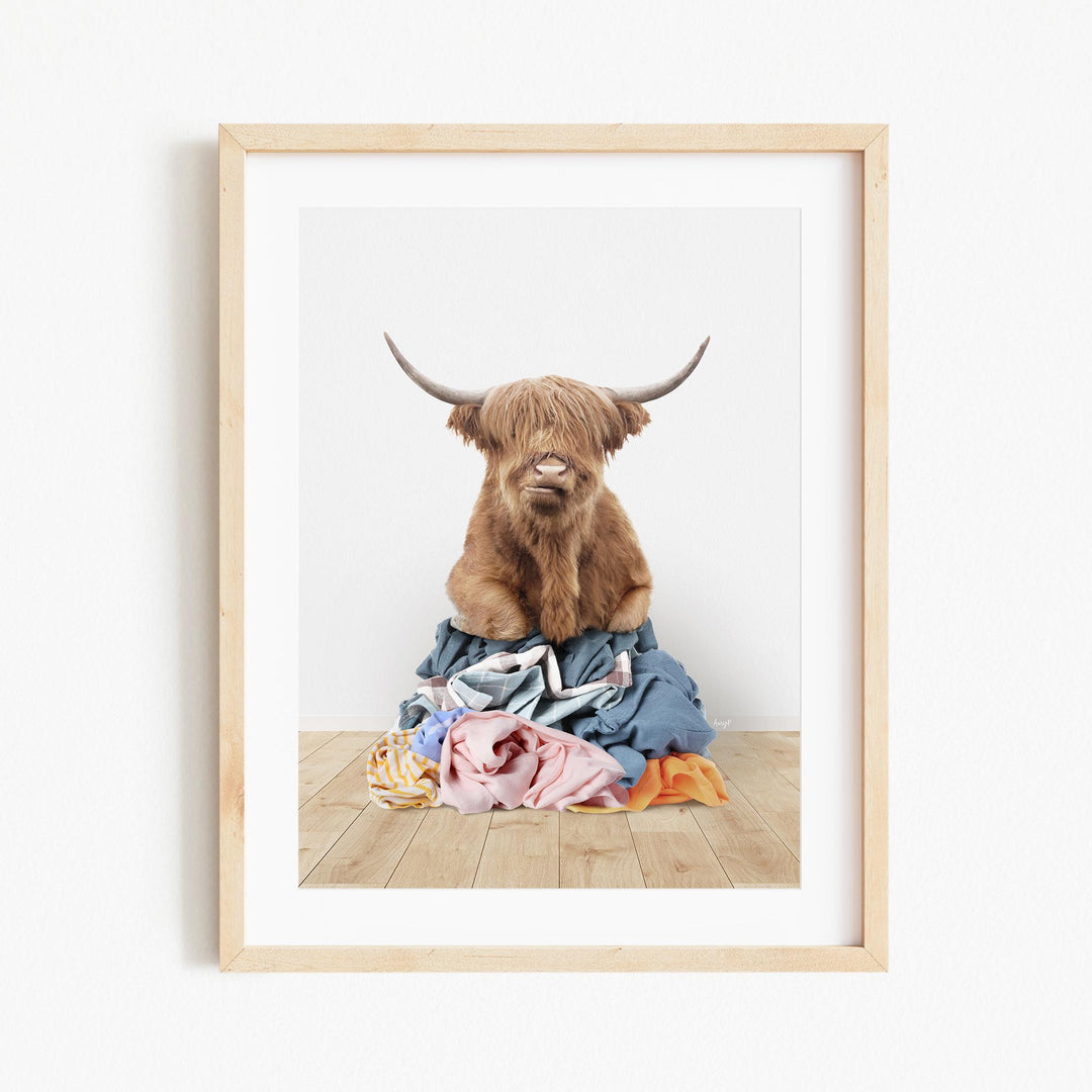 A brown Highland cow with long horns is sitting on a pile of clothes in the center of the image.