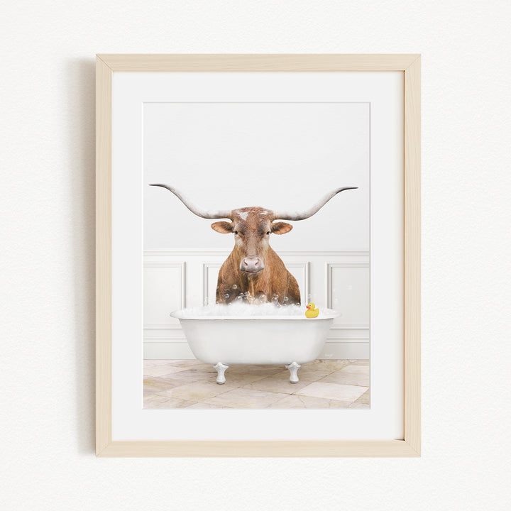 A brown cow with long horns is sitting in a white bathtub filled with water, with a yellow rubber duck floating in the water.