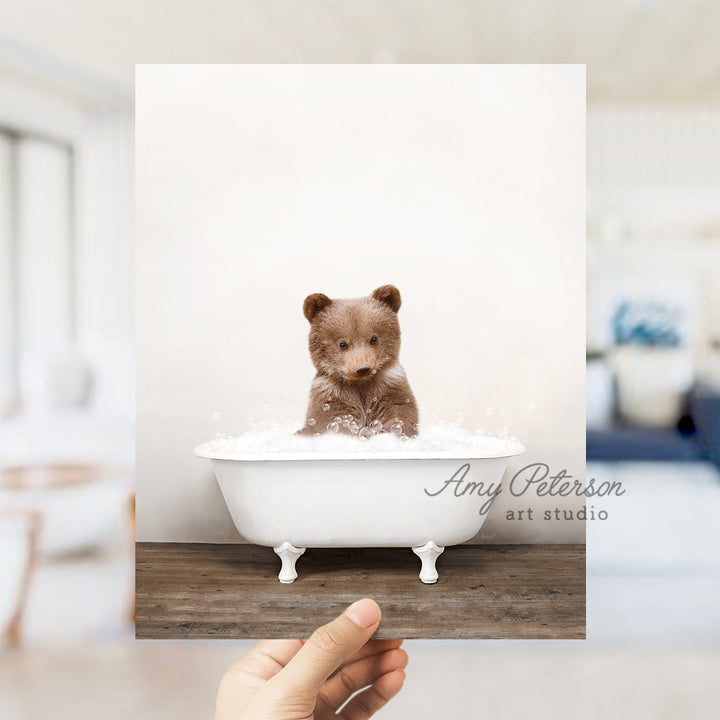 a hand holding a photo of a teddy bear in a bathtub