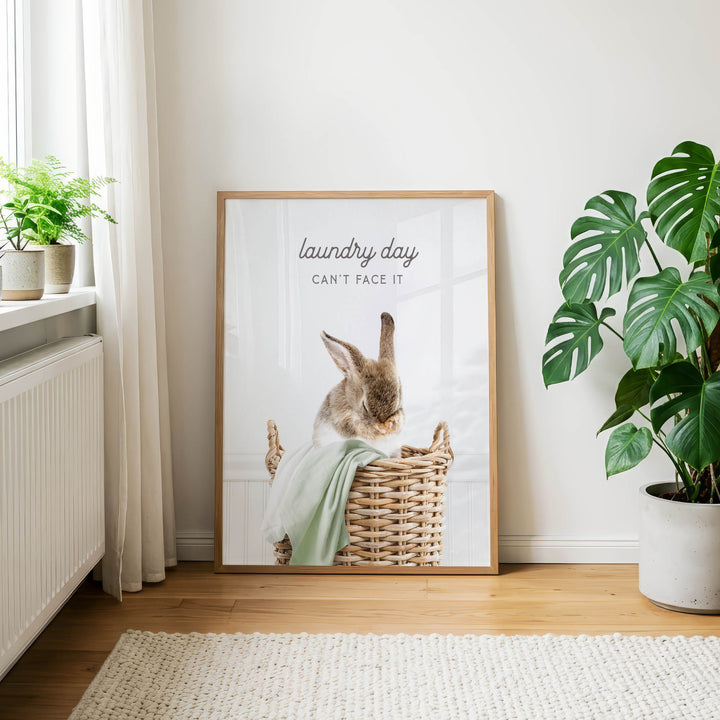 A framed poster of a rabbit sitting in a wicker basket, with the text "laundry day can't face it" displayed on the poster.