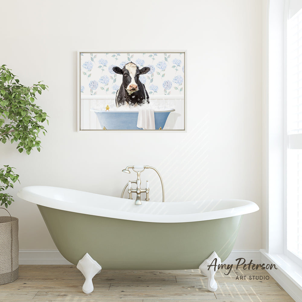 A green clawfoot bathtub with a framed cow image above it, set against a white wall with a window and a potted plant.
