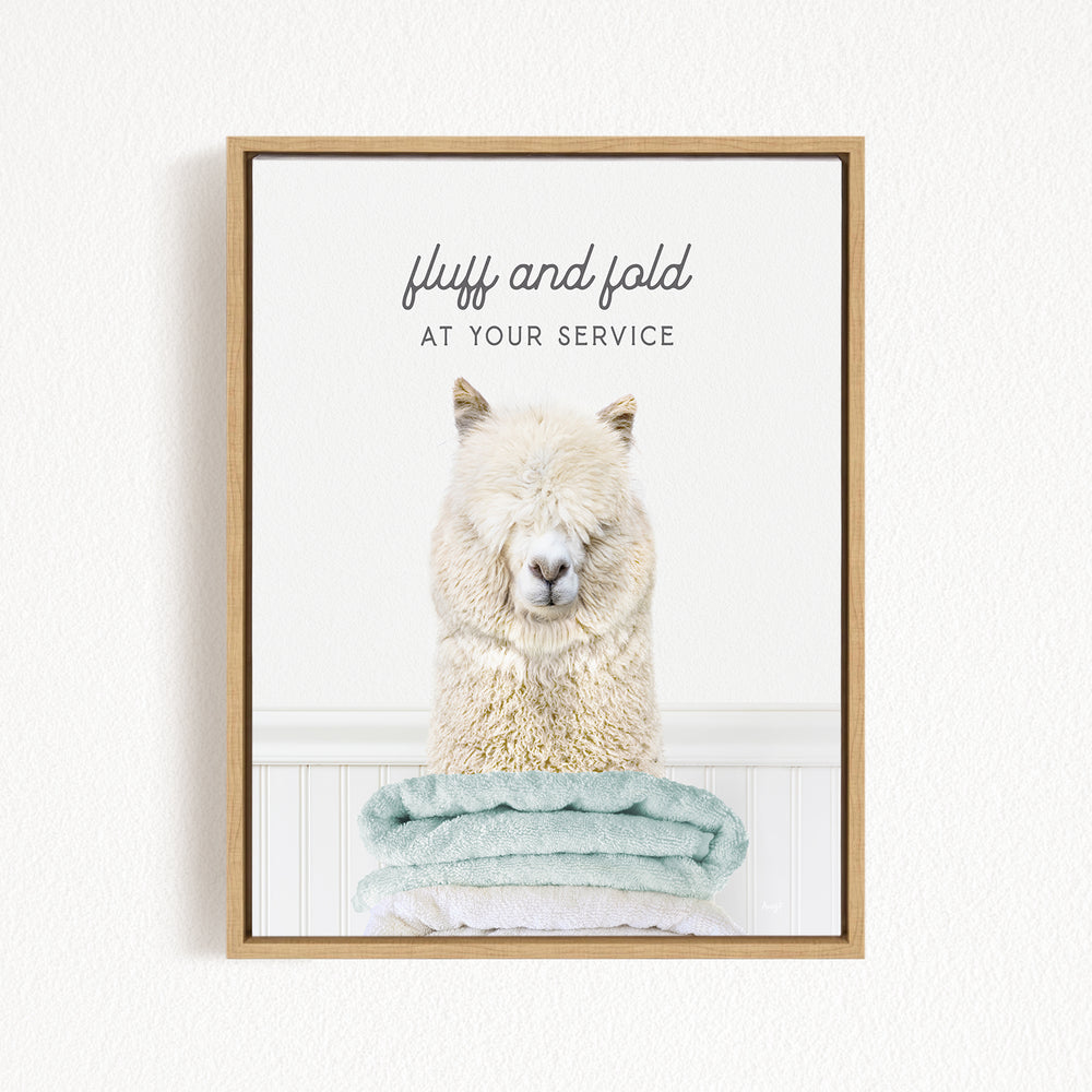 A fluffy white alpaca sitting on a stack of light blue towels, with the text "fluff and fold at your service" written above the image.