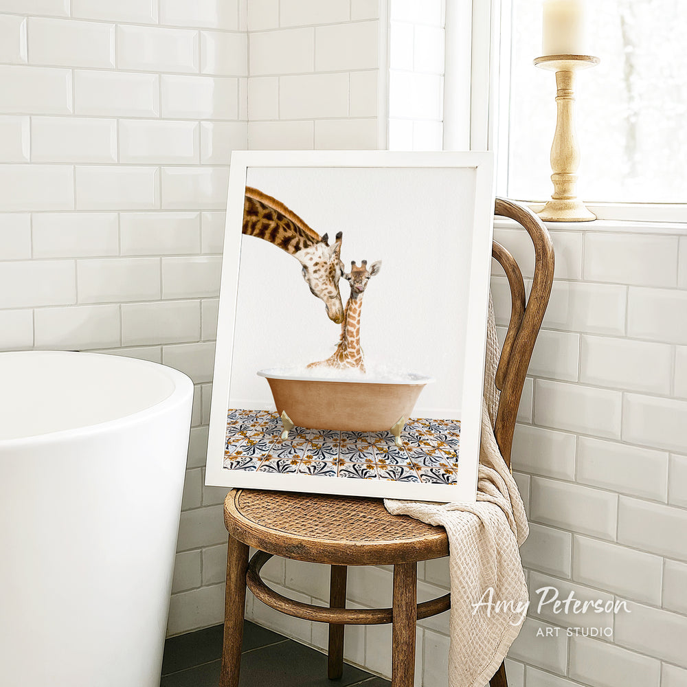 A framed image of a giraffe and a baby giraffe sitting in a bathtub, with a towel draped over the back of a wooden chair in a bathroom setting.