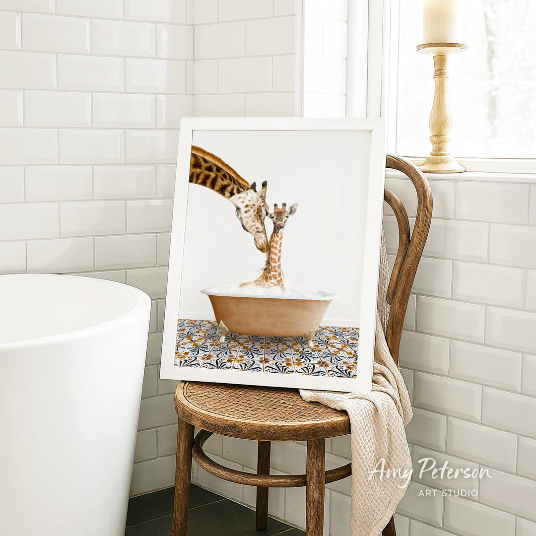 A framed image of a giraffe and a baby giraffe sitting in a bathtub, with a towel draped over the back of a wooden chair in a bathroom setting.